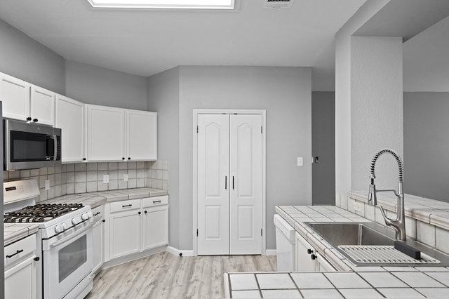 kitchen with tile counters, light wood-style flooring, white appliances, white cabinetry, and a sink