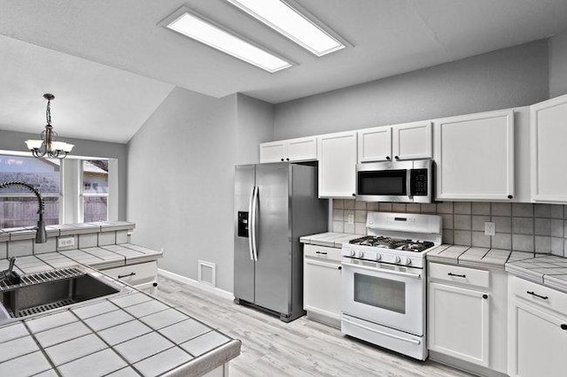 kitchen with a sink, decorative backsplash, tile counters, white cabinets, and appliances with stainless steel finishes