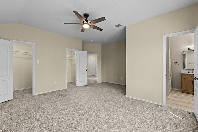 unfurnished bedroom featuring visible vents, baseboards, lofted ceiling, a walk in closet, and light colored carpet