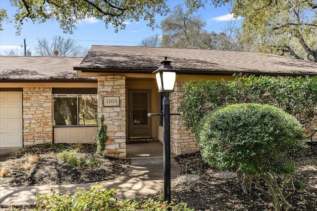 doorway to property featuring stone siding and roof with shingles