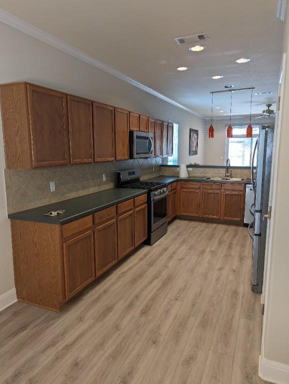 kitchen with visible vents, brown cabinets, ornamental molding, a sink, and appliances with stainless steel finishes