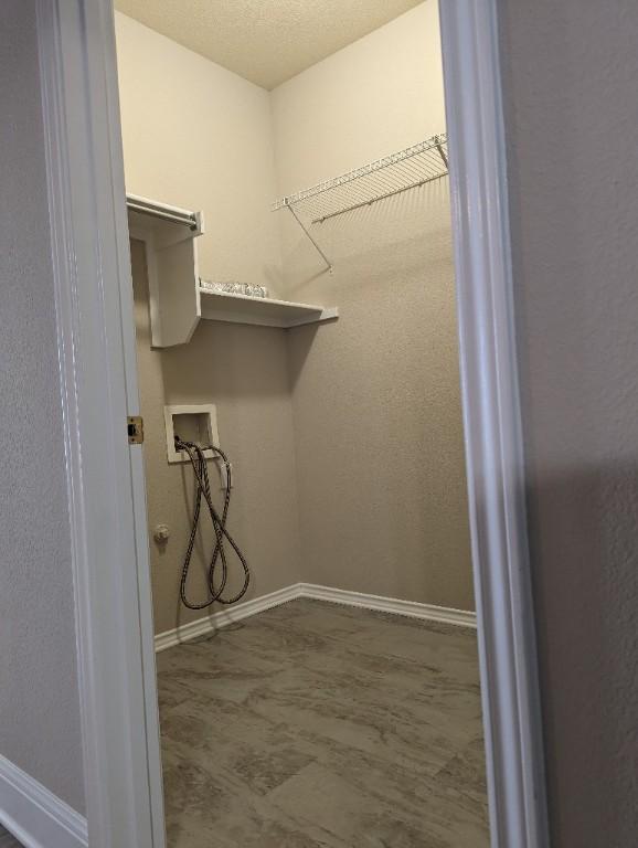 clothes washing area with laundry area, hookup for a washing machine, a textured ceiling, and baseboards