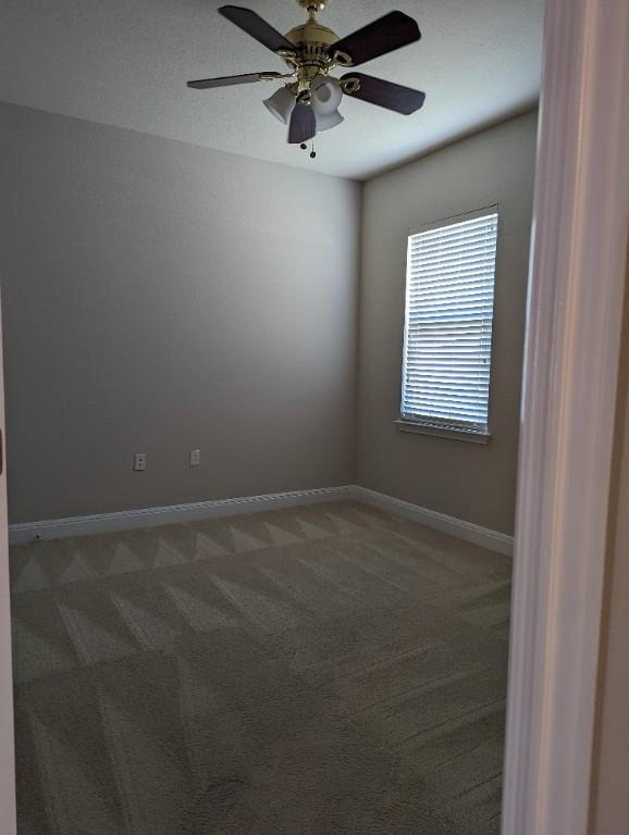 spare room featuring light colored carpet, baseboards, and ceiling fan