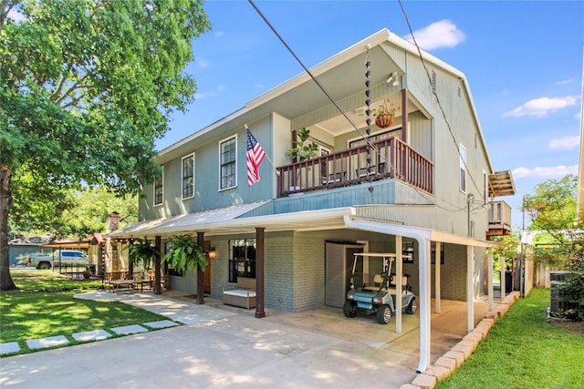 back of property with brick siding, a lawn, a balcony, a carport, and driveway