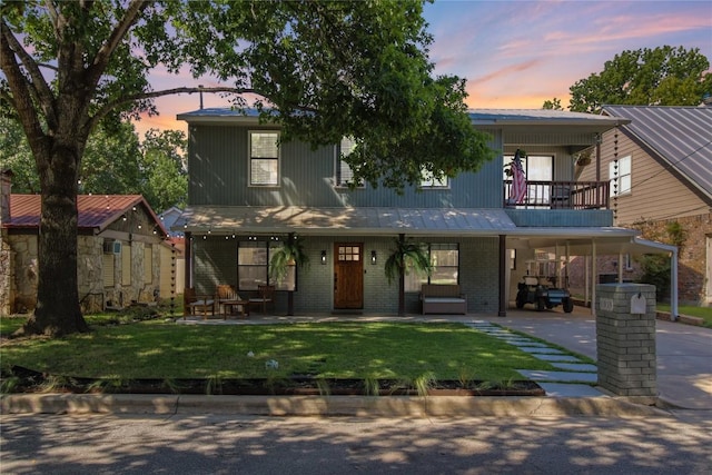 view of front of home with brick siding, a front lawn, metal roof, a balcony, and driveway