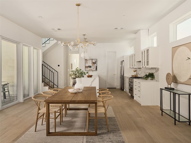 dining space featuring visible vents, an inviting chandelier, stairway, and light wood-style floors