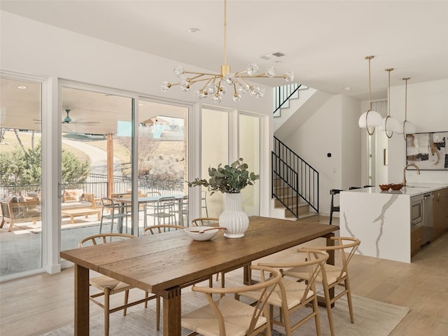 dining space with ceiling fan with notable chandelier, stairway, light wood-style floors, and visible vents