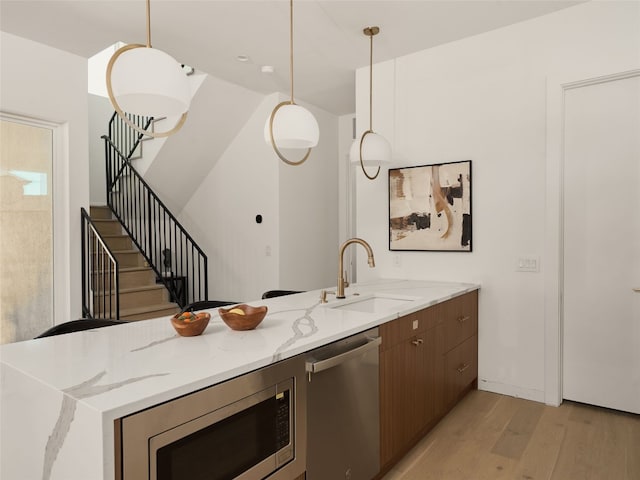 kitchen featuring a sink, light stone counters, light wood-style floors, and stainless steel appliances