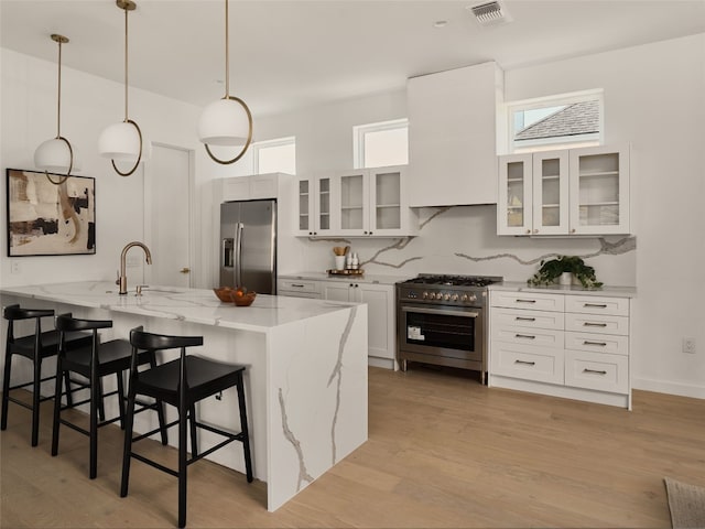 kitchen with light stone countertops, visible vents, stainless steel appliances, light wood-style floors, and a kitchen bar