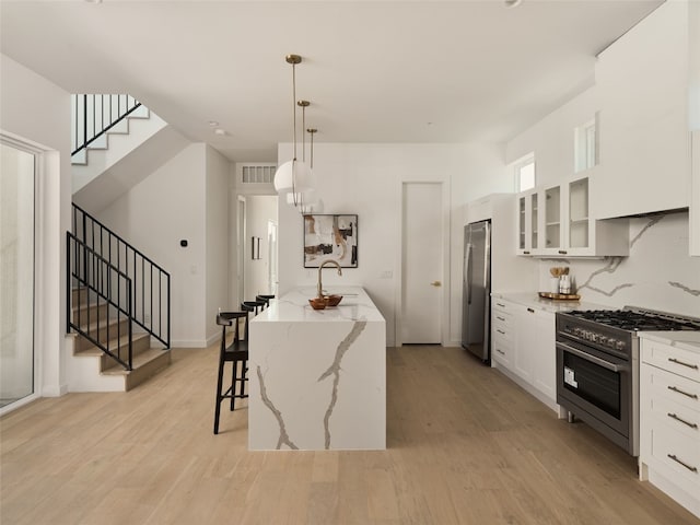 kitchen with glass insert cabinets, light wood-style flooring, stainless steel appliances, and a kitchen bar