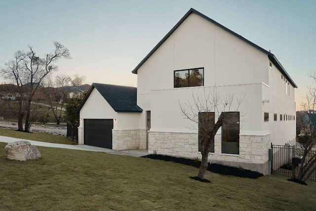 property exterior at dusk with stone siding, a lawn, a garage, and stucco siding