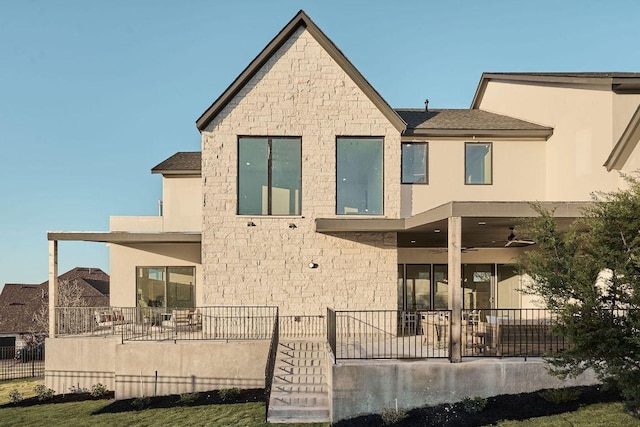 back of property with a patio area, stone siding, stucco siding, and fence