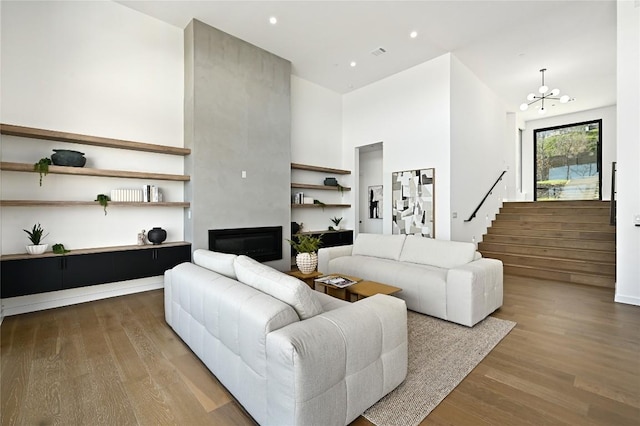 living room featuring a notable chandelier, wood finished floors, a fireplace, a towering ceiling, and stairs