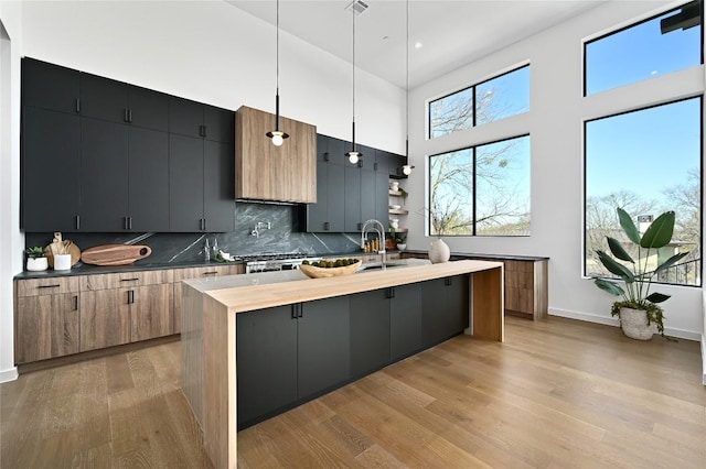 kitchen with a kitchen island with sink, tasteful backsplash, light wood-style floors, baseboards, and a towering ceiling