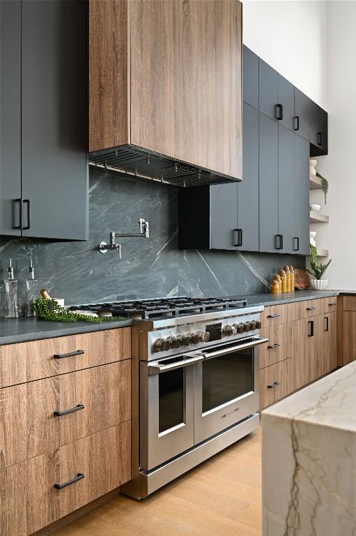 kitchen with tasteful backsplash, double oven range, light wood-style floors, custom exhaust hood, and modern cabinets