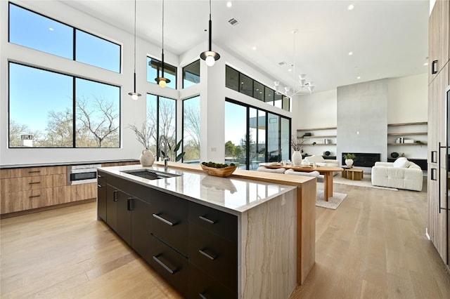 kitchen featuring visible vents, modern cabinets, a center island with sink, a sink, and light wood-style floors