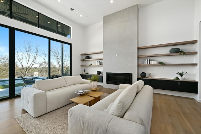 living room featuring visible vents, a large fireplace, recessed lighting, a high ceiling, and wood finished floors