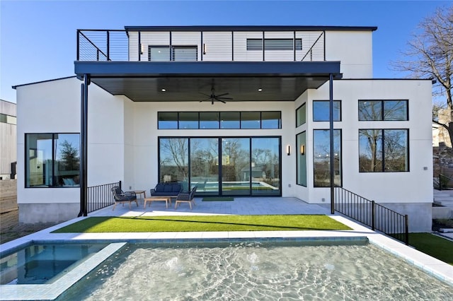 rear view of property with a patio, a balcony, a ceiling fan, an in ground hot tub, and stucco siding