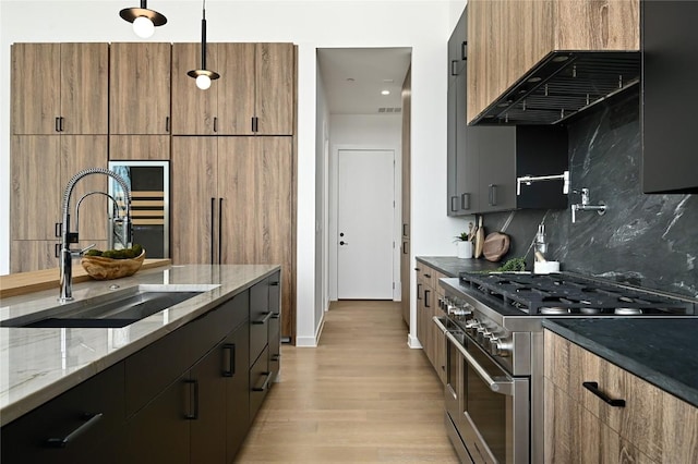 kitchen with light stone countertops, range with two ovens, a sink, light wood-style floors, and backsplash