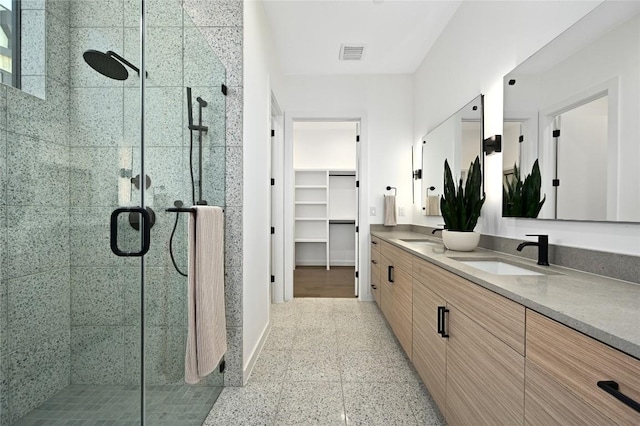 full bath featuring visible vents, double vanity, a stall shower, a sink, and a spacious closet