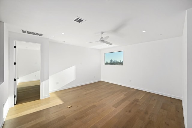 unfurnished room with a ceiling fan, wood finished floors, visible vents, and baseboards