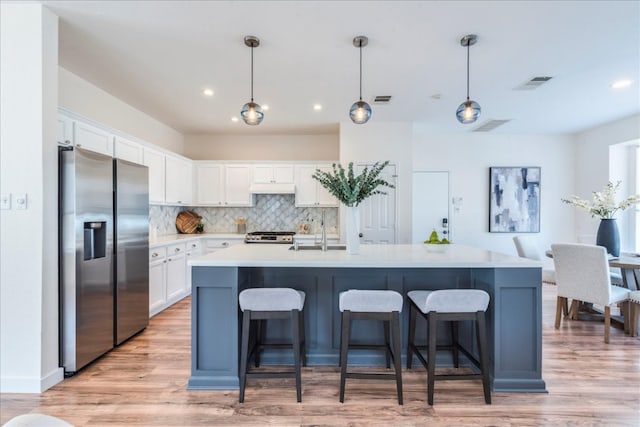 kitchen with visible vents, under cabinet range hood, white cabinets, stainless steel fridge, and a sink