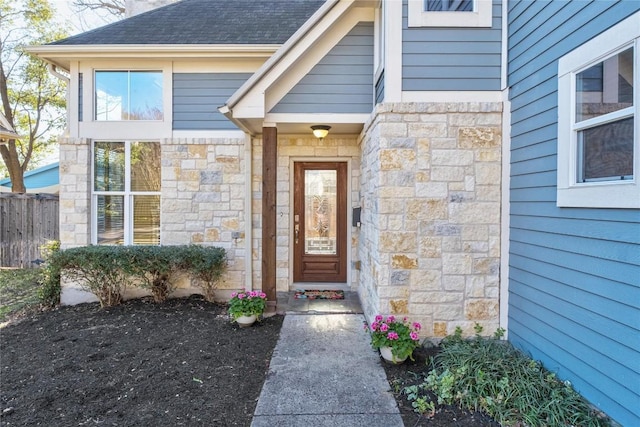 property entrance with stone siding, fence, and a shingled roof