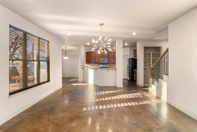 kitchen with stainless steel microwave, an inviting chandelier, concrete floors, and freestanding refrigerator