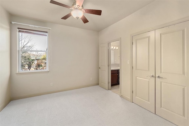 unfurnished bedroom featuring ensuite bath, a closet, baseboards, light colored carpet, and ceiling fan