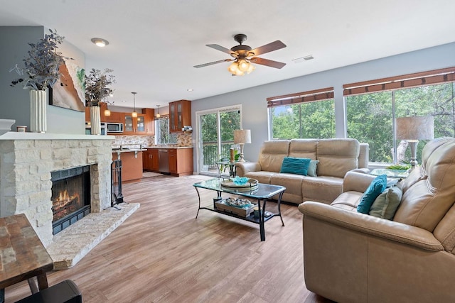 living area with a ceiling fan, light wood-style flooring, a fireplace, and visible vents