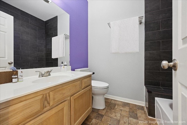 bathroom featuring stone finish flooring, baseboards, toilet, a bathtub, and vanity