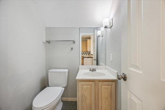 bathroom with toilet, vanity, and a textured wall