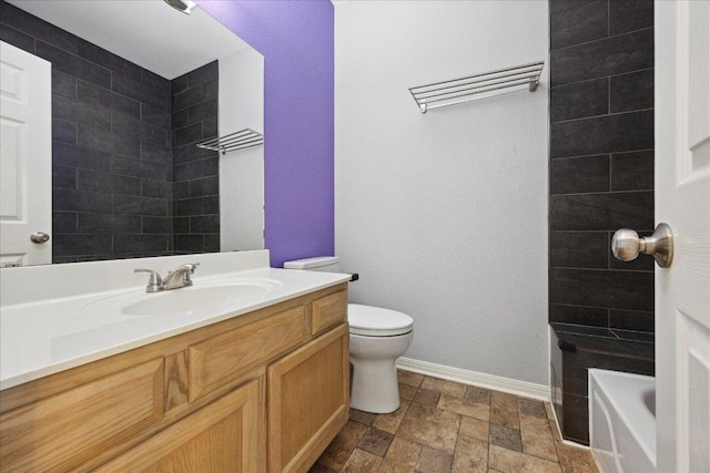 bathroom featuring a tub, stone finish flooring, baseboards, toilet, and vanity