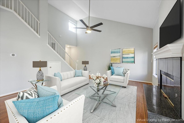 living room featuring a fireplace with flush hearth, stairs, wood finished floors, high vaulted ceiling, and a ceiling fan