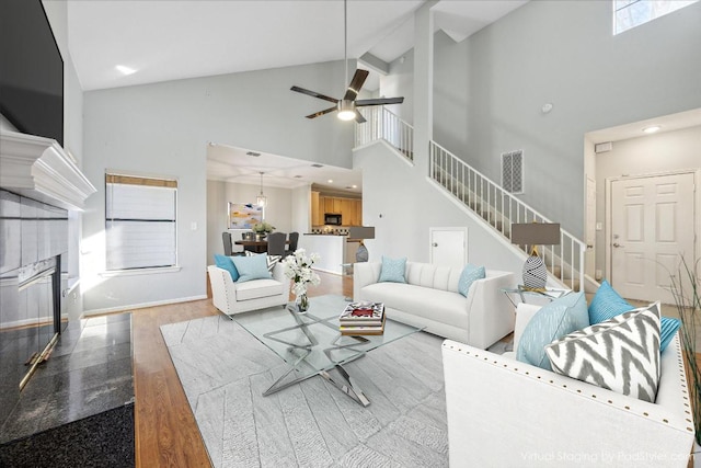 living area with high vaulted ceiling, a ceiling fan, wood finished floors, stairway, and a fireplace