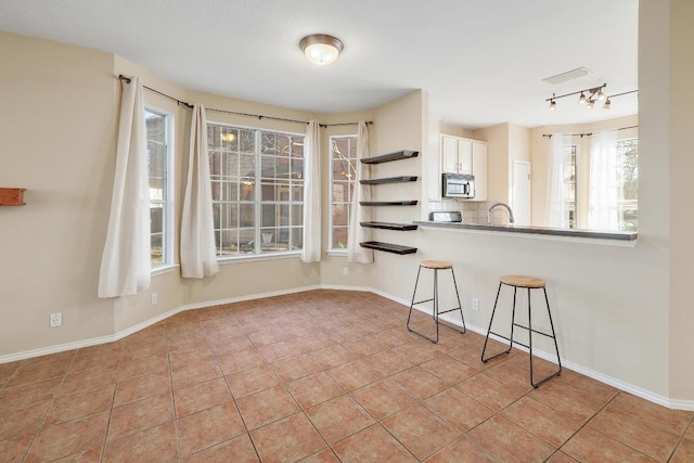 kitchen with stainless steel microwave, a breakfast bar area, light tile patterned flooring, white cabinets, and open shelves