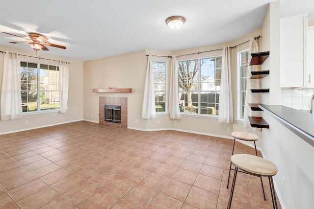 unfurnished living room featuring light tile patterned flooring, a healthy amount of sunlight, baseboards, and a tile fireplace