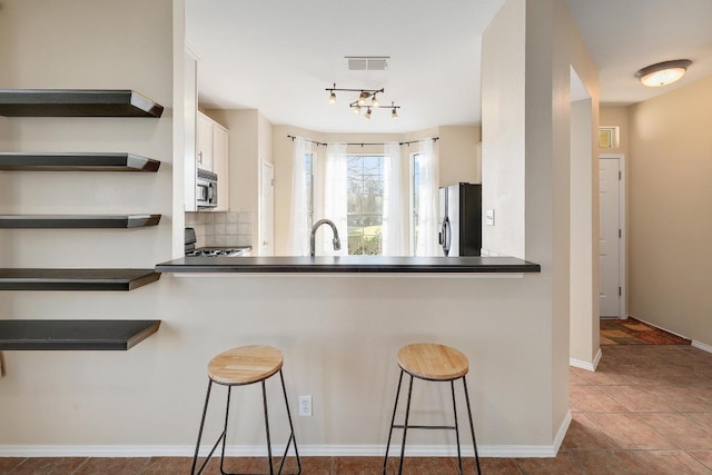 kitchen featuring stainless steel appliances, dark countertops, open shelves, and a breakfast bar