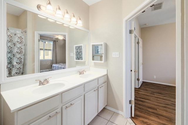 bathroom with double vanity, ensuite bath, baseboards, and wood finished floors