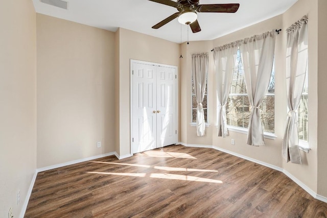 empty room featuring ceiling fan, visible vents, baseboards, and wood finished floors