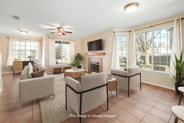 living area with baseboards, a tiled fireplace, tile patterned floors, and a ceiling fan