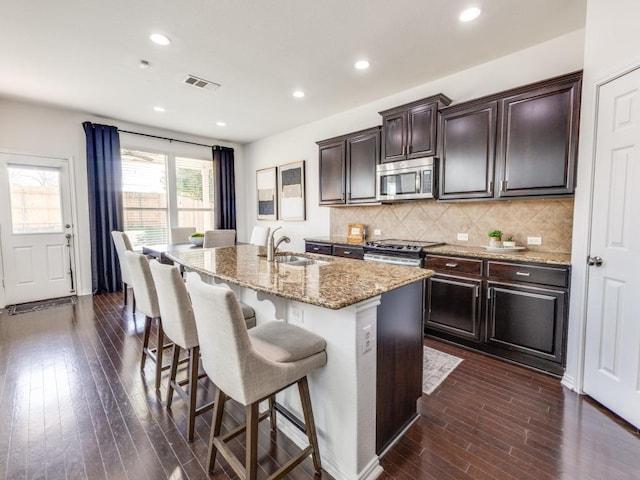 kitchen with light stone counters, dark wood-style floors, a sink, stainless steel appliances, and tasteful backsplash