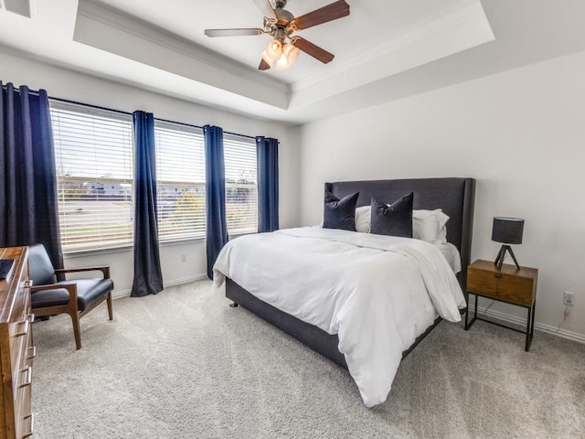 bedroom with crown molding, baseboards, ceiling fan, light colored carpet, and a raised ceiling