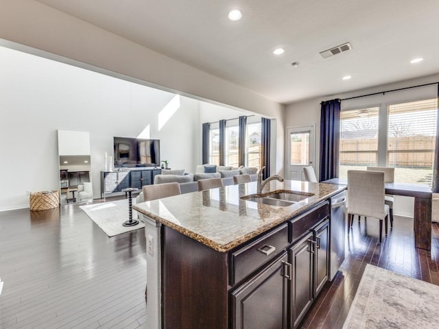 kitchen with visible vents, a sink, stainless steel dishwasher, dark wood-style floors, and light stone countertops