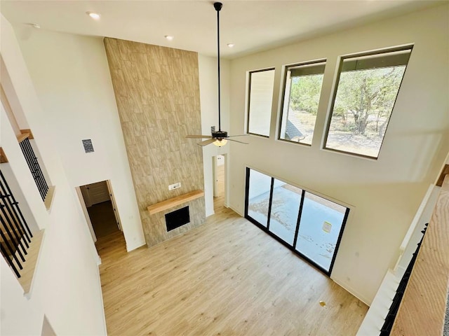 1670 Headwaters Blvd, Dripping Springs, TX 78620 - unfurnished living room with a high ceiling, light wood-style floors, a large fireplace, plenty of natural light, and a ceiling fan