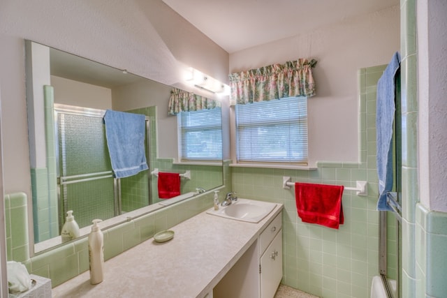 full bath featuring a shower with door, a wainscoted wall, tile walls, and vanity