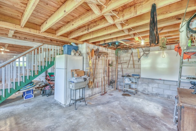 unfinished below grade area with stairs, concrete block wall, and freestanding refrigerator