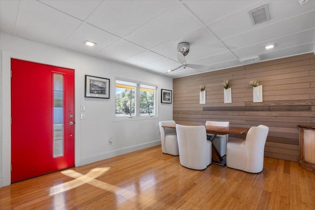 dining room featuring wooden walls, baseboards, visible vents, a paneled ceiling, and light wood-type flooring