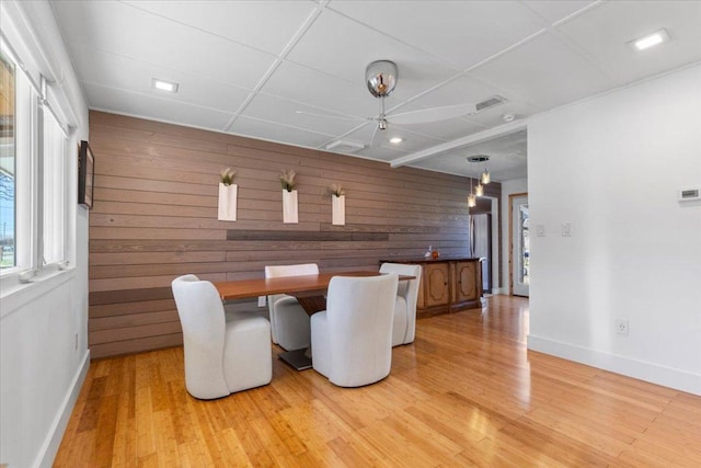 dining area with light wood-type flooring, visible vents, wood walls, a paneled ceiling, and baseboards