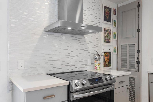 kitchen with decorative backsplash, light countertops, wall chimney range hood, and stainless steel range with electric cooktop